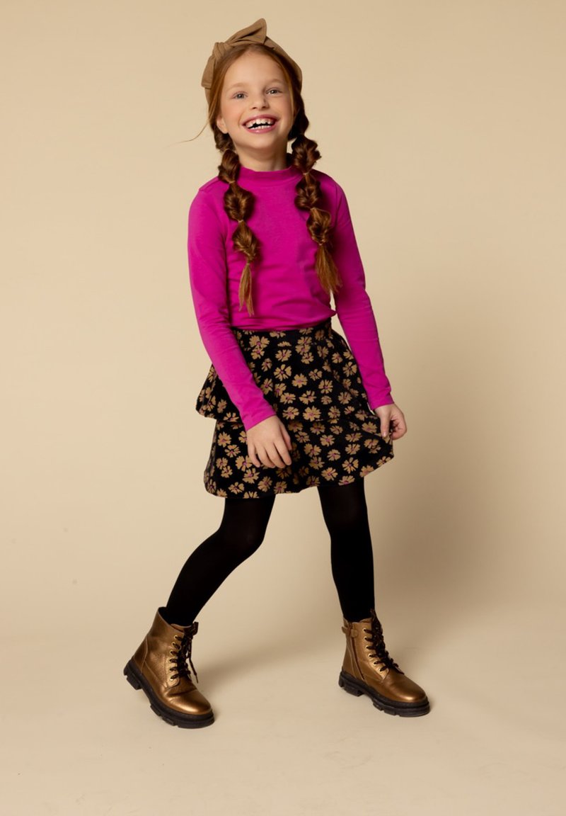 Roze lange mouwen top, zwarte bloemenrok met ruffles, zwarte panty’s en glanzende gouden combatlaarzen. Bruin strik hoofdtooi accentueert de stijl.
