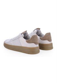 Baskets en cuir blanc avec un accent en suède beige au talon, un col rembourré et une semelle en caoutchouc beige à surface texturée.