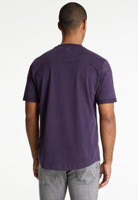 Tamsiai violetinė trumpa rankovė marškinėliai su apvaliu apvadu ir plokščiu siūlių detalizavimu pečiuose, pagaminti iš minkštos medvilnės mišinio.