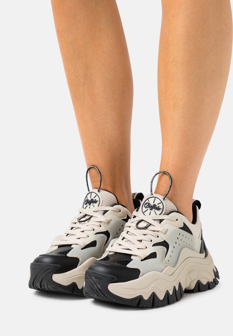 Grube sneakersy wykonane z mieszanki beżowych, czarnych i białych materiałów, z teksturowaną podeszwą, perforowanymi akcentami i pętlami do łatwego zakładania.