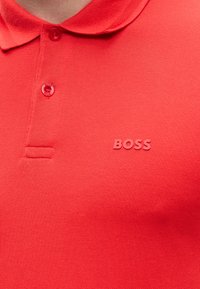 Polo rouge avec col, deux boutons (dont un marqué "BOSS") et logo "BOSS" en relief sur la poitrine.