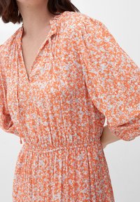 Pomarańczowa i jasnoniebieska sukienka w kwiatowy wzór z dekoltem w kształcie V, z dopasowaną talią i balonowymi rękawami, uszyta z lekkiego materiału.