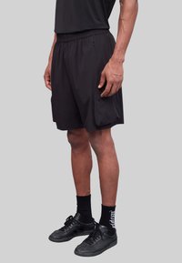 Shorts de sport noirs avec une taille élastique et des poches latérales, fabriqués en matériau léger. Portés avec des baskets noires et des chaussettes.