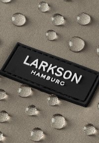 Bežová tkanina s vyvýšenými kvapkami a textúrovaným povrchom; obsahuje čiernu obdĺžnikovú nálepku s bielym textom "LARKSON HAMBURG."