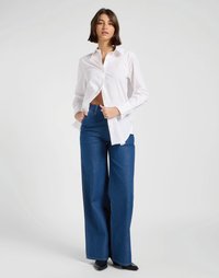 Camisa branca de botões com colarinho, combinada com jeans de ganga azul de perna larga. Sapatos pretos de bico fino completam o visual. Design simples e limpo.