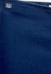 Mörkblått tyg med en sydd fåll och en liten vit broderad "PB"-logotyp i det övre vänstra hörnet.