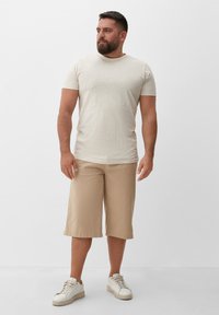 Beige katoenen t-shirt met korte mouwen, gecombineerd met beige knielange shorts. Model draagt witte sneakers; minimalistisch ontwerp en lichte textuur.