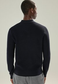 Navyfarbener strukturierter Strickpullover mit langen Ärmeln, einem Rippkragen und einem Rippbund. Verfügt über ein Karomuster und eine klassische Passform.