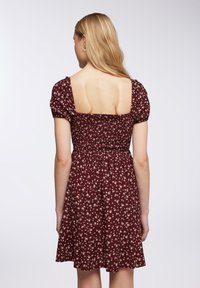 Vestito corto color bordeaux con schiena quadrata, maniche a sbuffo, vita elastica e piccolo motivo floreale su tutto il tessuto.