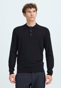 Cămașă polo neagră cu mânecă lungă, cu guler, cinci nasturi și un design ajustat. Fabricată dintr-un material neted, prezintă o textură subtilă.