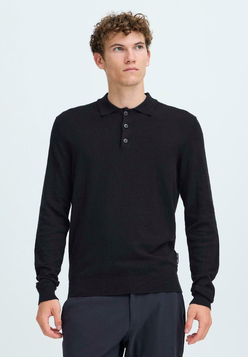 Cămașă polo neagră cu mânecă lungă, cu guler, cinci nasturi și un design ajustat. Fabricată dintr-un material neted, prezintă o textură subtilă.