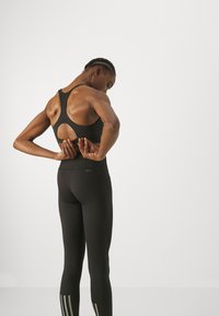 Svart sports-bh med utskjært rygg, parret med svarte leggings med subtile grå striper ved anklene. Elegant, tettsittende design.