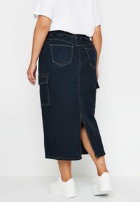 Dżinsowa spódnica midi w ciemnoniebieskim kolorze, z elastycznym paskiem w talii, dwoma tylnymi kieszeniami, kieszenią typu cargo po bokach oraz rozcięciem z tyłu dla ułatwienia ruchu.