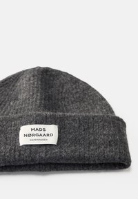 Bonnet tricoté gris avec un revers. Présente une étiquette blanche avec le texte "MADS NØRGAAARD COPENHAGEN". Texture douce, design simple.