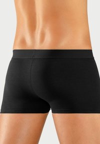 Juodi bokso šortai, pagaminti iš minkštos medžiagos, su lygiu juosmeniu ir tvirtu prigludimu, minimalistinio dizaino, be matomų raštų.