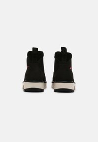 Black suede ankle boots featuring a cream sole, sturdy design, and a pull tab on the back for easy wear. Red logo detail on the side.