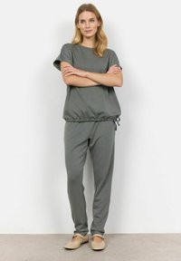Grå to-delt outfit bestående af en kortærmet top med indsnøring i taljen og matchende bukser med en afslappet pasform, lavet af blødt stof.