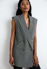 Harmaa raitapaita ilman hihoja, syvällä V-kaula-aukolla, kaksirivisellä suunnittelulla, suurilla napeilla ja vyökoristella vyötäröllä.