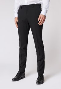 Pantaloni neri con vestibilità sartoriale, realizzati in tessuto leggero e liscio. Presentano un davanti piatto e passanti per cintura, abbinati a scarpe in pelle nere.