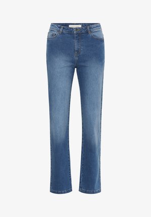 Kvinde med krøllet hår, iført en navy- og hvidstribet kortærmet top, blå jeans med lige ben og sorte balletsko, står med den ene hånd på hoften.