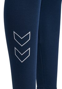 Leggings azul marino hechos de una tela suave y elástica, con patrones de líneas en zigzag blancas en el muslo externo. Textura suave, diseño ajustado.