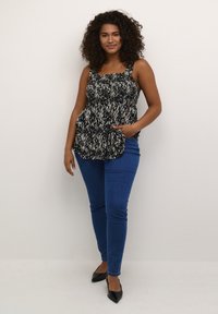 Mustvalge mustriga peplum-top, laiade rihmadega, smockitud bodice ja laienev hems, koos siniste kitsaste teksade ja mustade teravate kingadega.