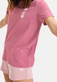 Růžové bavlněné tričko s květinovým vzorem a krátkými rukávy, spárované se světle růžovými bavlněnými šortkami s malým logem na lemu.