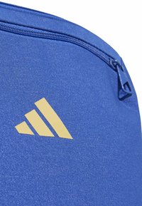 Detailný záber modrej textílie so žltým trojprúžkovým logom a modrým zipsom na taške alebo puzdre.