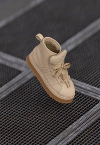 Sneaker alta beige in pelle liscia, con superficie testurizzata, vestibilità aderente, lacci prominenti e suola in gomma beige.