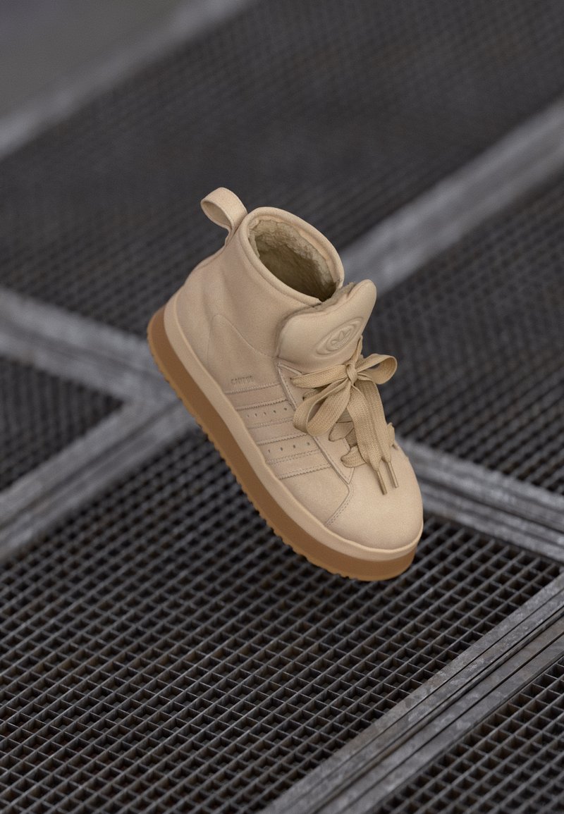 Sneaker alta beige in pelle liscia, con superficie testurizzata, vestibilità aderente, lacci prominenti e suola in gomma beige.