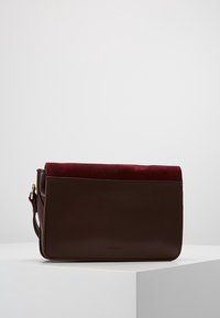Brun läderväska med en bordeauxfärgad mockaflap. Rektangulär form, minimalistisk design med axelrem och detaljer i guldton.