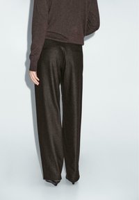 Pantalons noirs amples avec un léger éclat, design à l'avant plat et deux poches arrière, associés à un pull sombre.