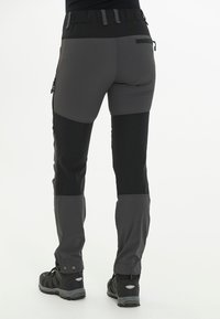 Zwarte en grijze outdoor broek met een aansluitend ontwerp, voorzien van ritszakken en rekbaar materiaal voor flexibiliteit en comfort.