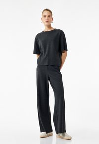 Ein dunkelgraues, verkürztes T-shirt und ein weitgeschnittene Hose Set, aus einem weichen Stoff gefertigt. Verfügt über eine lässige Passform und minimale Nähte für mehr Komfort.