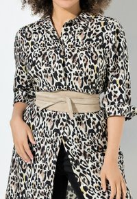 Košilové šaty s leopardím vzorem, s knoflíkovým zapínáním, dlouhými rukávy a zavázaným béžovým opaskem v oblasti pasu. Hladká tkanina s kontrastními vzory.
