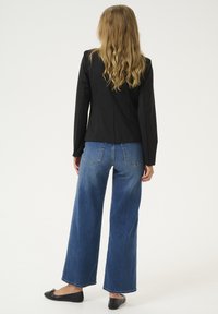 Schwarze taillierte Blazer kombiniert mit hoch geschnittenen, weit geschnittenen blauen Jeans, die ein zweifarbige Farbverlaufwäsche aufweisen. Schwarze Ballettschuhe runden das Outfit ab.