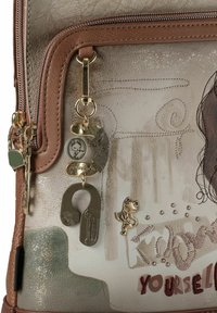 Mittelgroße Tasche aus beigem Kunstleder mit texturierter Oberfläche. Verfügt über goldfarbene Beschläge, Anhänger und bestickte Akzente in verschiedenen Farben.