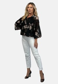 Czarna przezroczysta bluzka z kwiatowym wzorem, ze ściąganym dekoltem i szerokimi rękawami, zestawiona z białymi dopasowanymi spodniami i czarnymi koturnami.