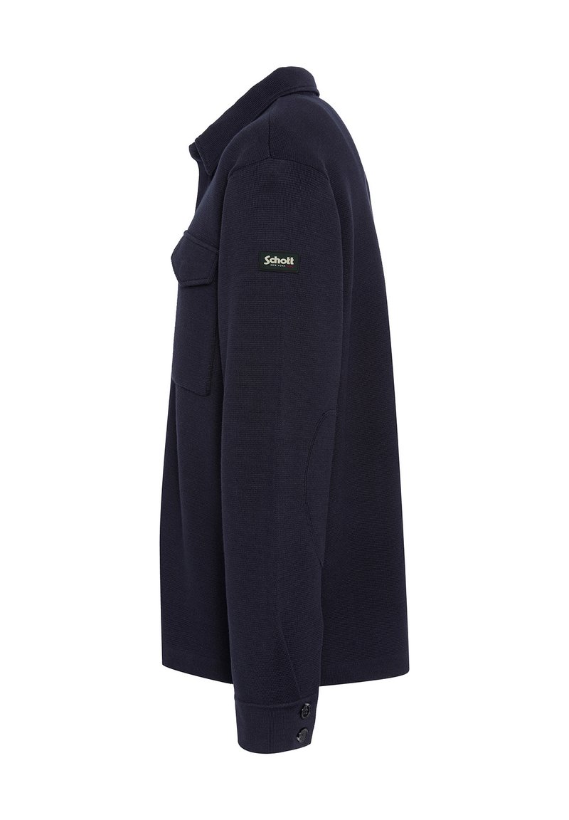Pull-over bleu marine en tissu texturé. Dispose d'un col, d'une poche poitrine et de poignets à boutons. Logo Schott sur l'épaule gauche.