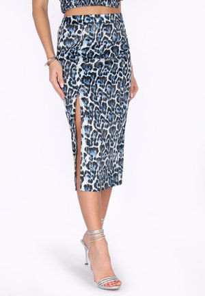 Frau trägt einen blau-schwarzen Rock in Leo-Print mit hohem Schlitz, kombiniert mit silbernen Riemchen-High Heels.
