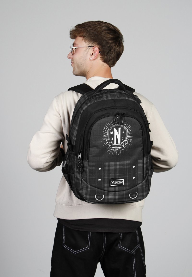 Mochila de cuadros negros con un logo, múltiples compartimentos y bolsillo lateral de malla. Hecha de material duradero con correas ajustables.