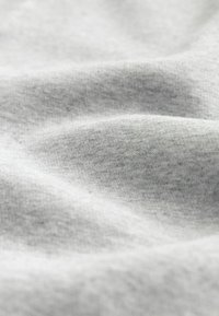 Tela gris claro con una textura suave que presenta pliegues sutiles y un aspecto ligeramente moteado, típico de material de algodón o jersey.