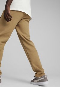 Pantaloni felpati color khaki con gambe affusolate, polsini a coste e tasche laterali, abbinati a sneakers grigie e bianche e una maglietta bianca.