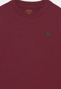Camiseta de manga corta burdeos hecha de algodón suave. Cuenta con un logo de pony bordado en verde en el pecho y un cuello redondo.