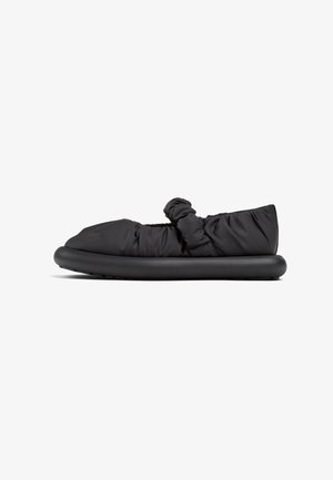 Sort polstret slip-on sko med sammensnøret stof og en knude detalje på overdelen, med en tyk sort sål for polstring og støtte.
