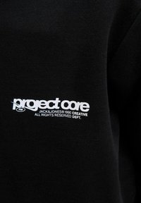 Felpa nera con texture a coste e un logo stampato bianco sul lato sinistro, con la scritta "project core" insieme ai dettagli del marchio.
