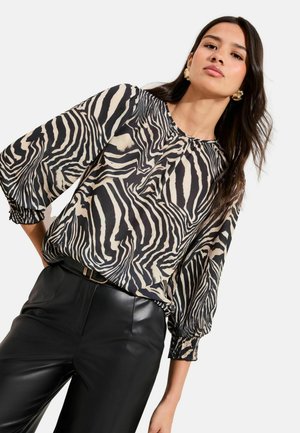 Black and beige zebra-patterned blouse with a round neckline and elastic cuffs, paired with high-waisted black leather pants.