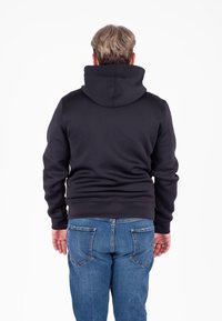Felpa nera con cappuccio, dal tessuto liscio, con polsini aderenti e una tasca a marsupio, abbinata a jeans in denim blu con due tasche posteriori.