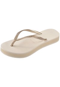 Flip-flop-sandaali, jossa on vaalea beige kumipohja, teksturoitu pohja ja metalliset kultaiset hihnat. Yksinkertainen muotoilu, jossa on vähän koristeita.