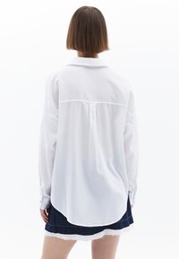 Witte lange mouwen blouse met een kraag, rugplooi-details en een afgeronde zoom, gecombineerd met een donkere spijkerrok met een rafelige zoom.